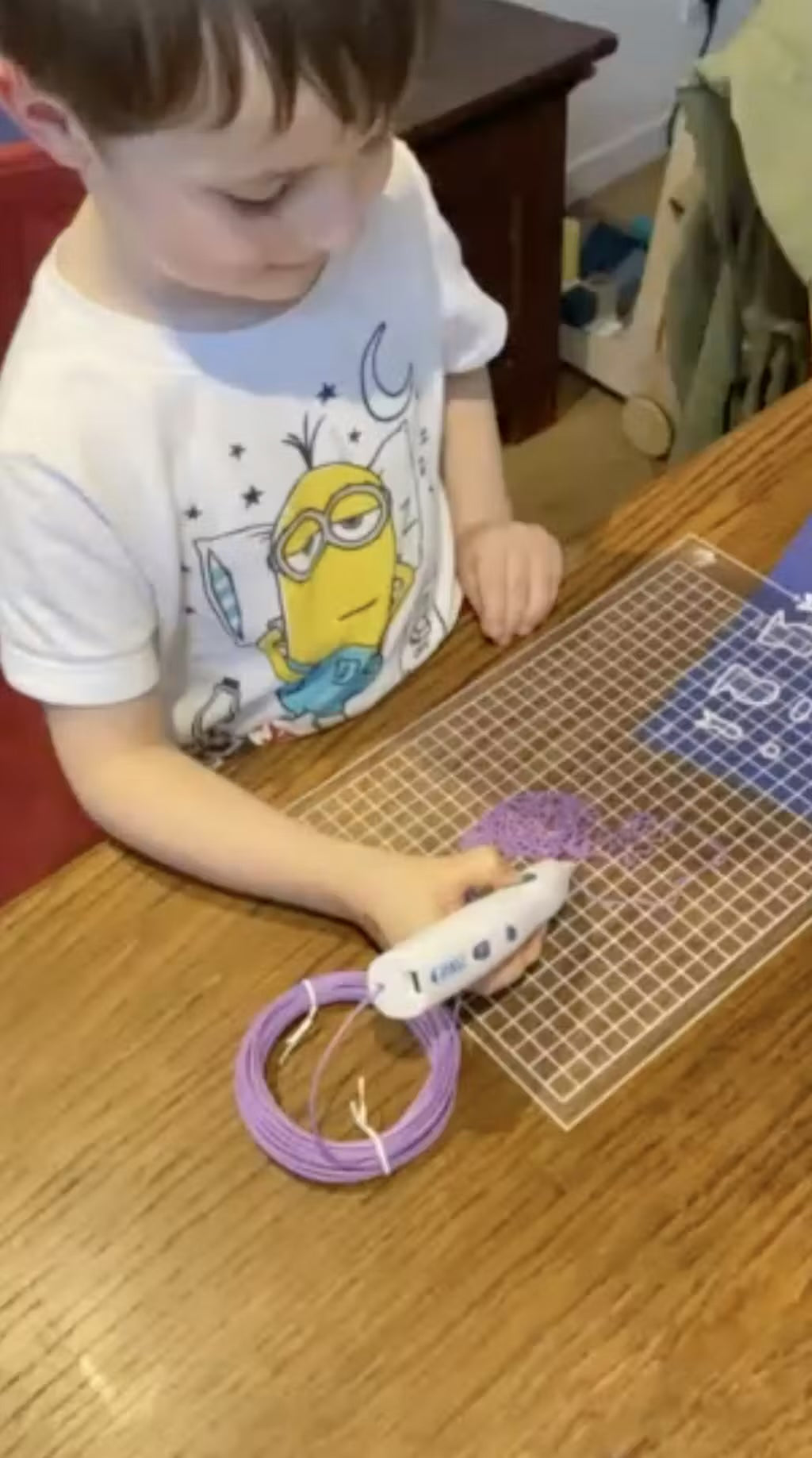 Un jeune garcon dessine au stylo 3D Pen'Up avec du filament violet sur une grille de travail