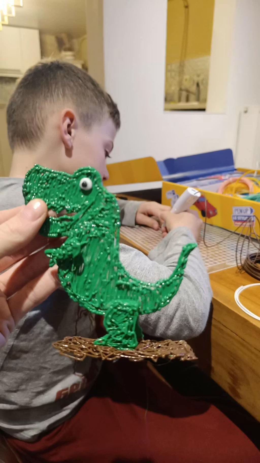 Un adulte presente un T-Rex vert realise au stylo 3D pendant qu'un garcon utilise le stylo Pen'Up